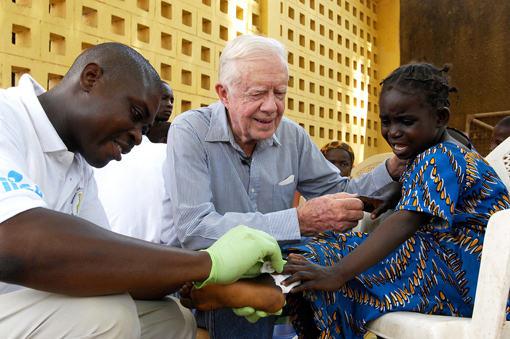 Former U.S. President Jimmy Carter tries to comfort 6-year-old Ruhama Issah at Savelugu Hospital as a Carter Center technical assistant dresses Issah's extremely painful Guinea worm wound.