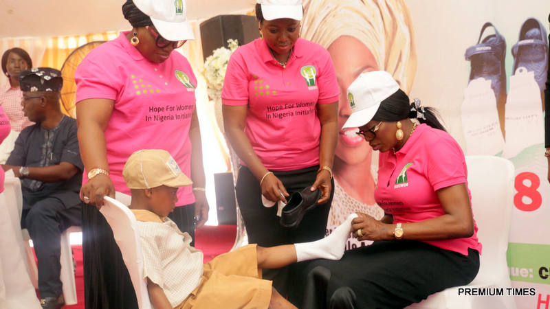Wife of Lagos State Governor & Founder of Hope for Women in Nigeria Initiative (HOFOWEM), Mrs. Bolanle Ambode (right), kitting one of the pupils of public primary schools in the State during the Flag-Off distribution of 50,000 shoes and socks, organised by the Foundation at Cherubim & Seraphim Primary School, Majidun, Ikorodu, on Tuesday, June 5, 2018. With them are C.EO, HOFOWEM, Mrs. Oyefunke Olayinka (2nd right) and a member of the HOFOWEM educational team.