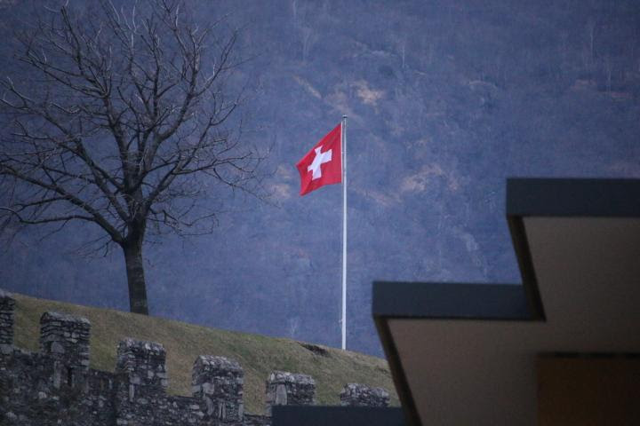 A Swiss Flag on a hill beneath a mountain in Bellinzona, Switzerland. New Narratives/James Harding Giahyue 