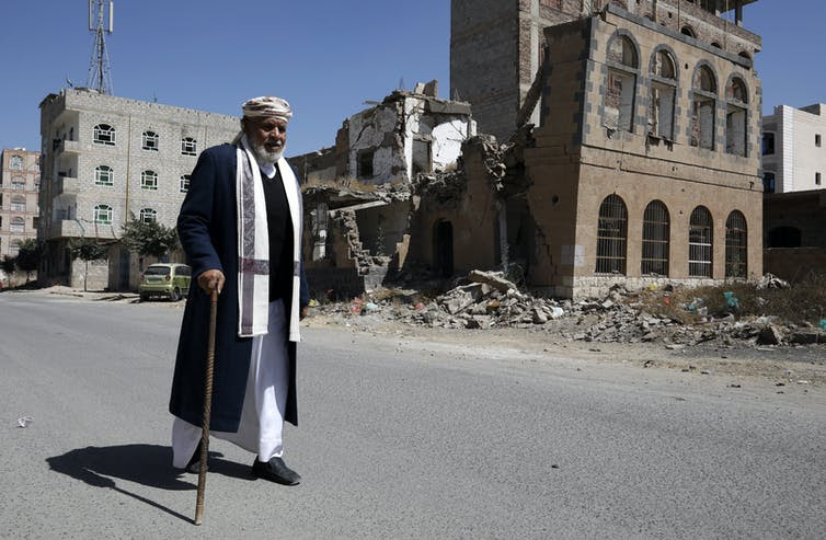 A man with a walking stick walks past a bombed building in Sana'a, Yemen, February 2021.Sana'a, Yemen, after a Saudi airstrike. EPA-EFE/Yahya Arhab